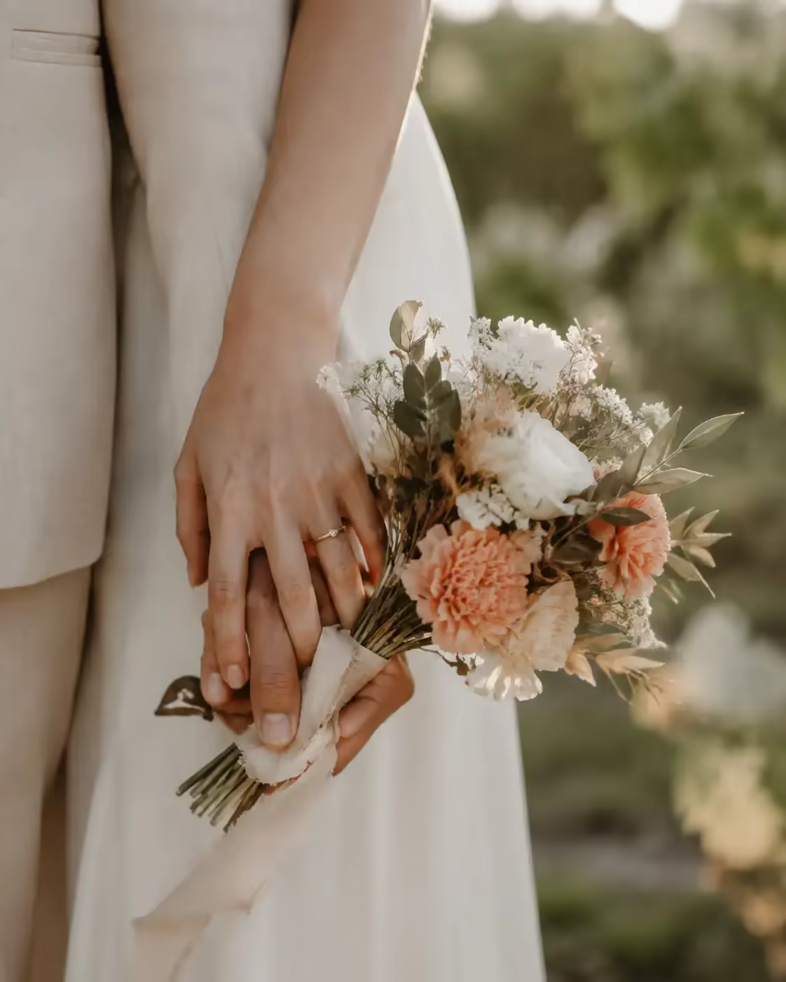 Mãos dos noivos junto a um ramo de casamento